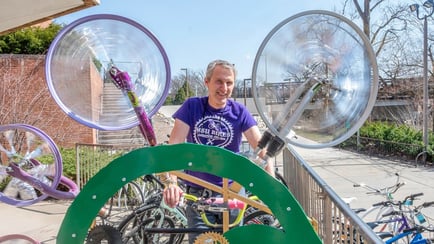 MSU bike expert Tim Potter stand behind a kinetic sculpture that features multiple spinning bike wheels in an arc.