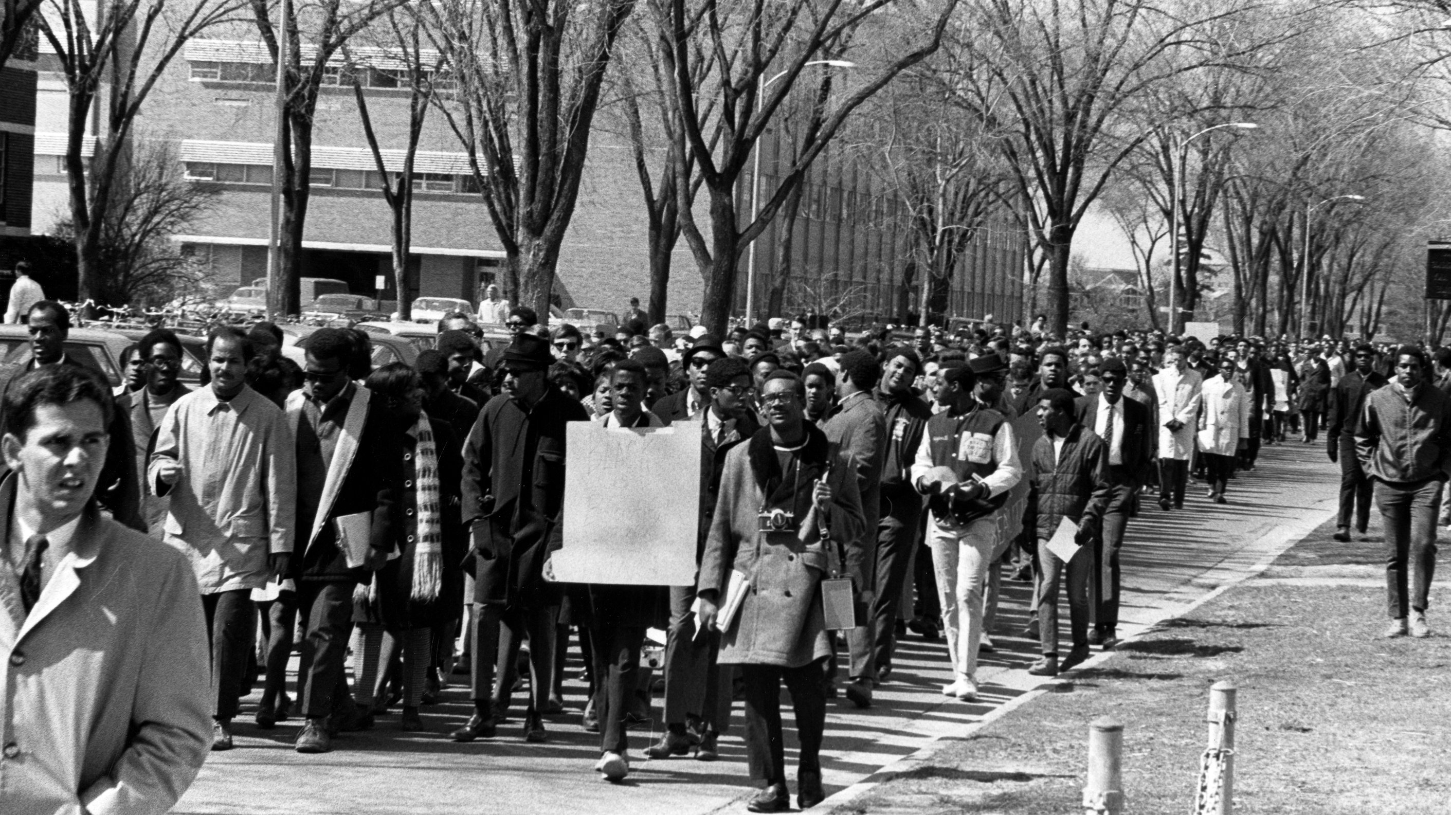 A black and white photo of students marching on a college campus.