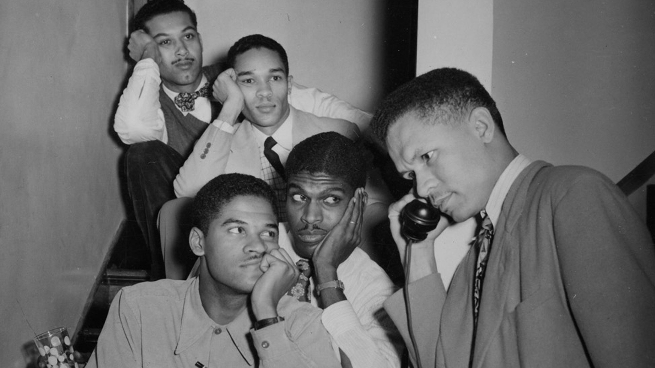 A black and white photo of men sitting on steps while one takes a phone call. 