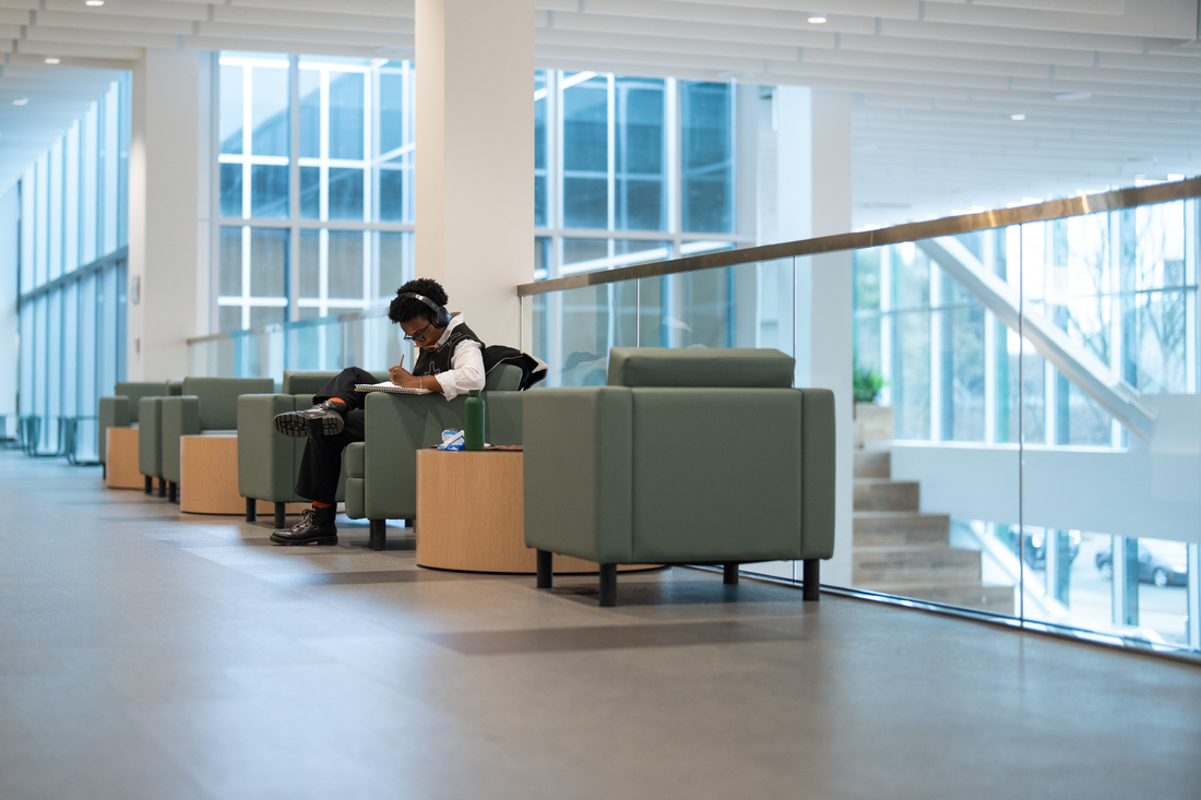 Four green chairs inside a building with a person sitting in one of them.