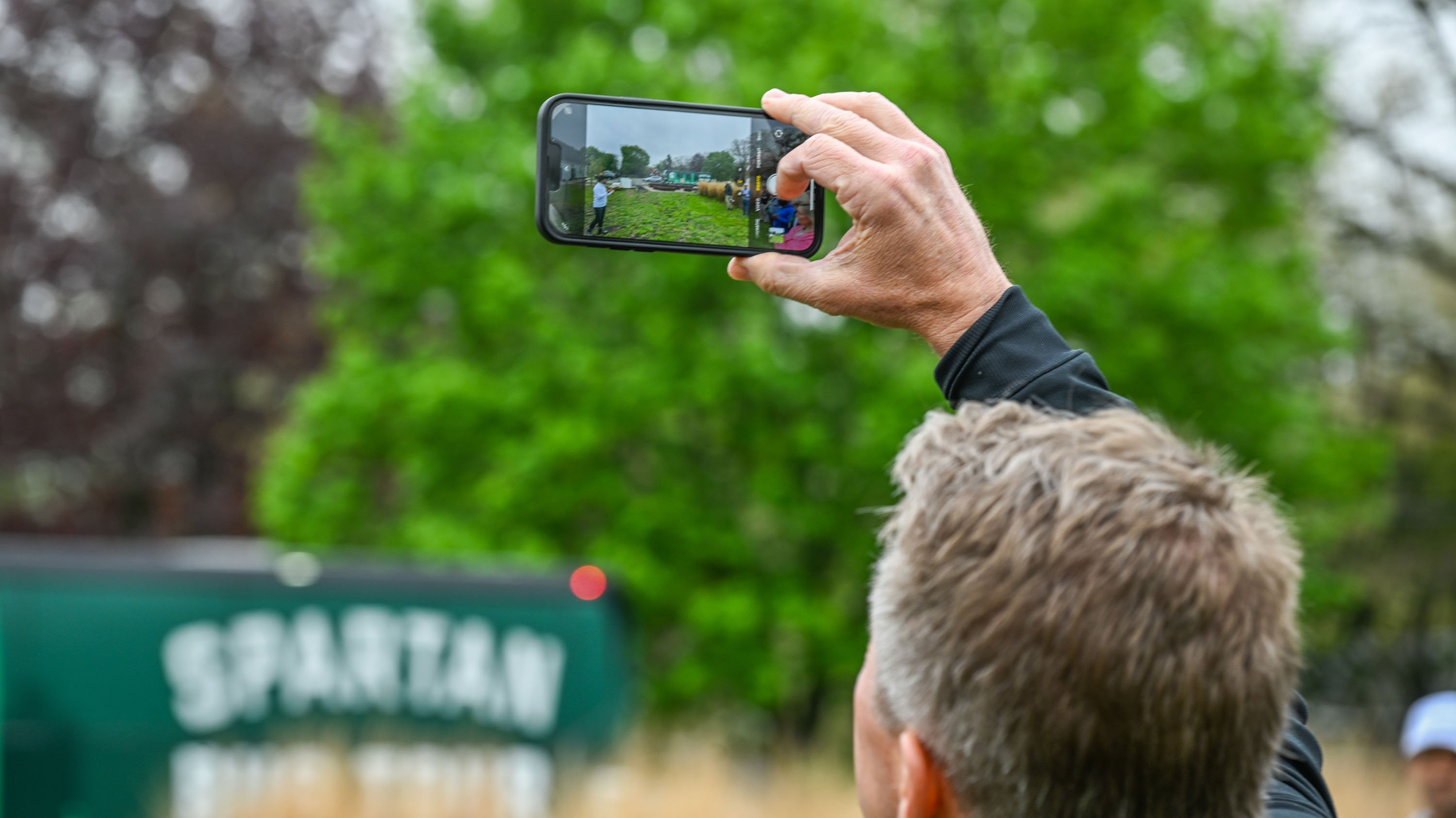 Close up of a person taking a photo of green space on their cell phone. 