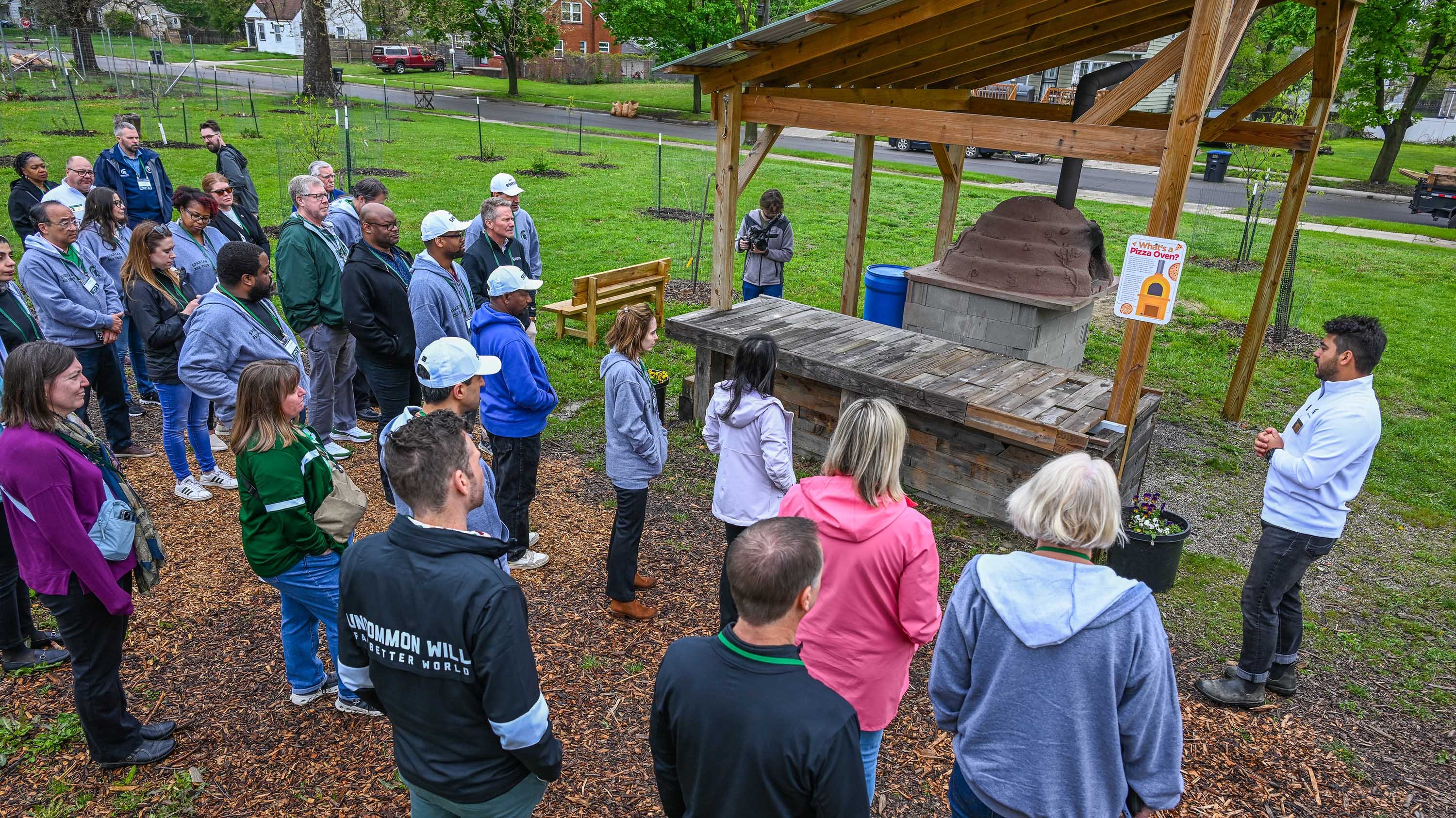 A group of people stand near a clay pizza oven.