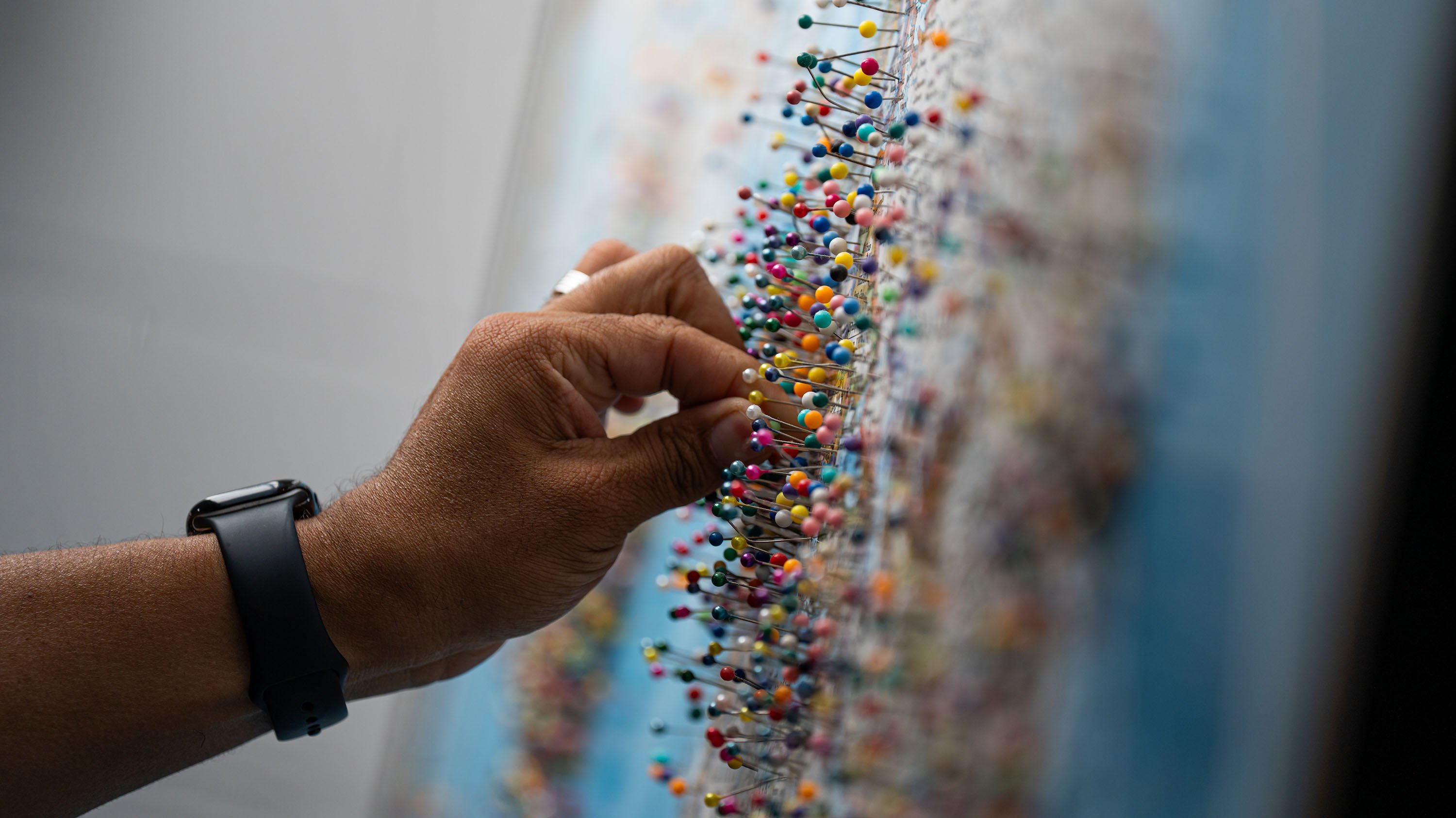 A hand puts a pin on a map. The map is covered in pins.