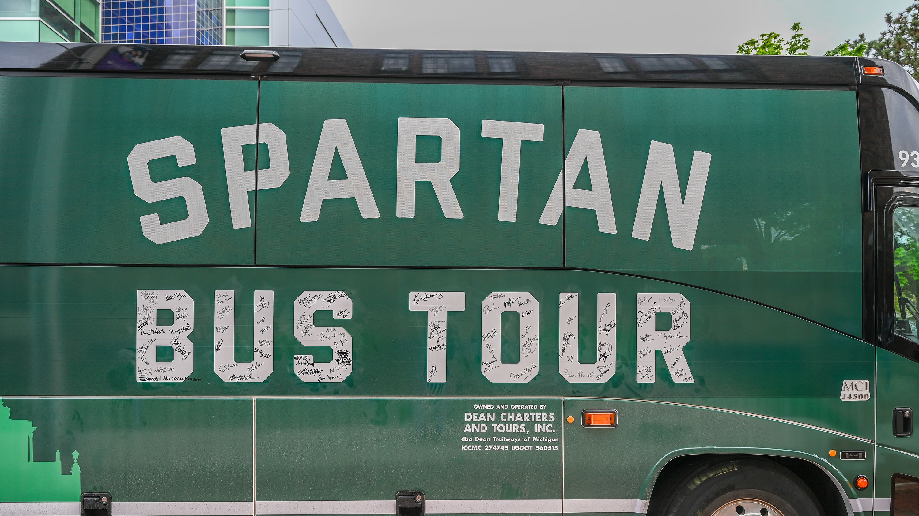A green bus with ?Spartan Bus Tour? written in white on the side. There are signatures inside the block letters of ?Spartan Bus Tour?