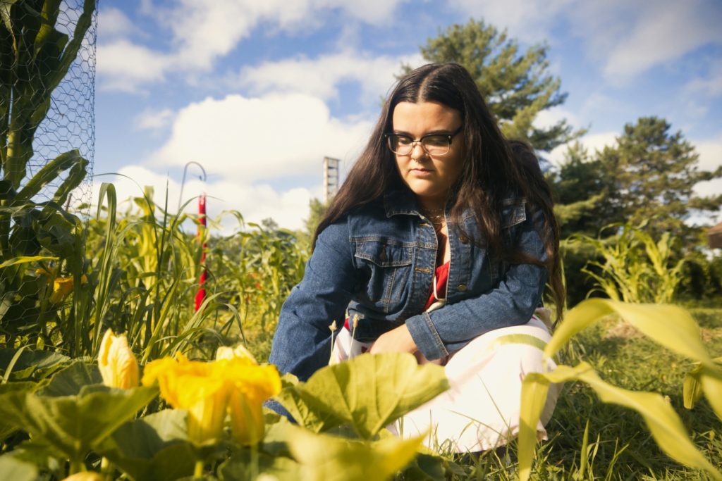 a woman crouched down in a garden in front of squash vines