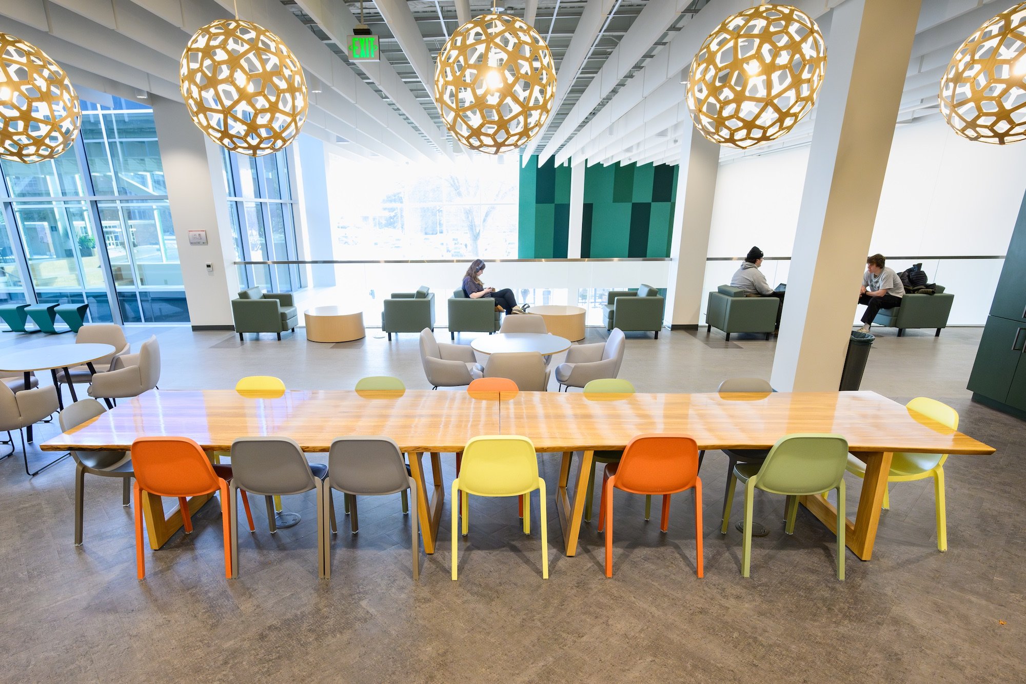 Lounge area with a long table and colorful chairs, surrounded by comfortable seating areas and distinctive pendant lights at the MSU Multicultural Center