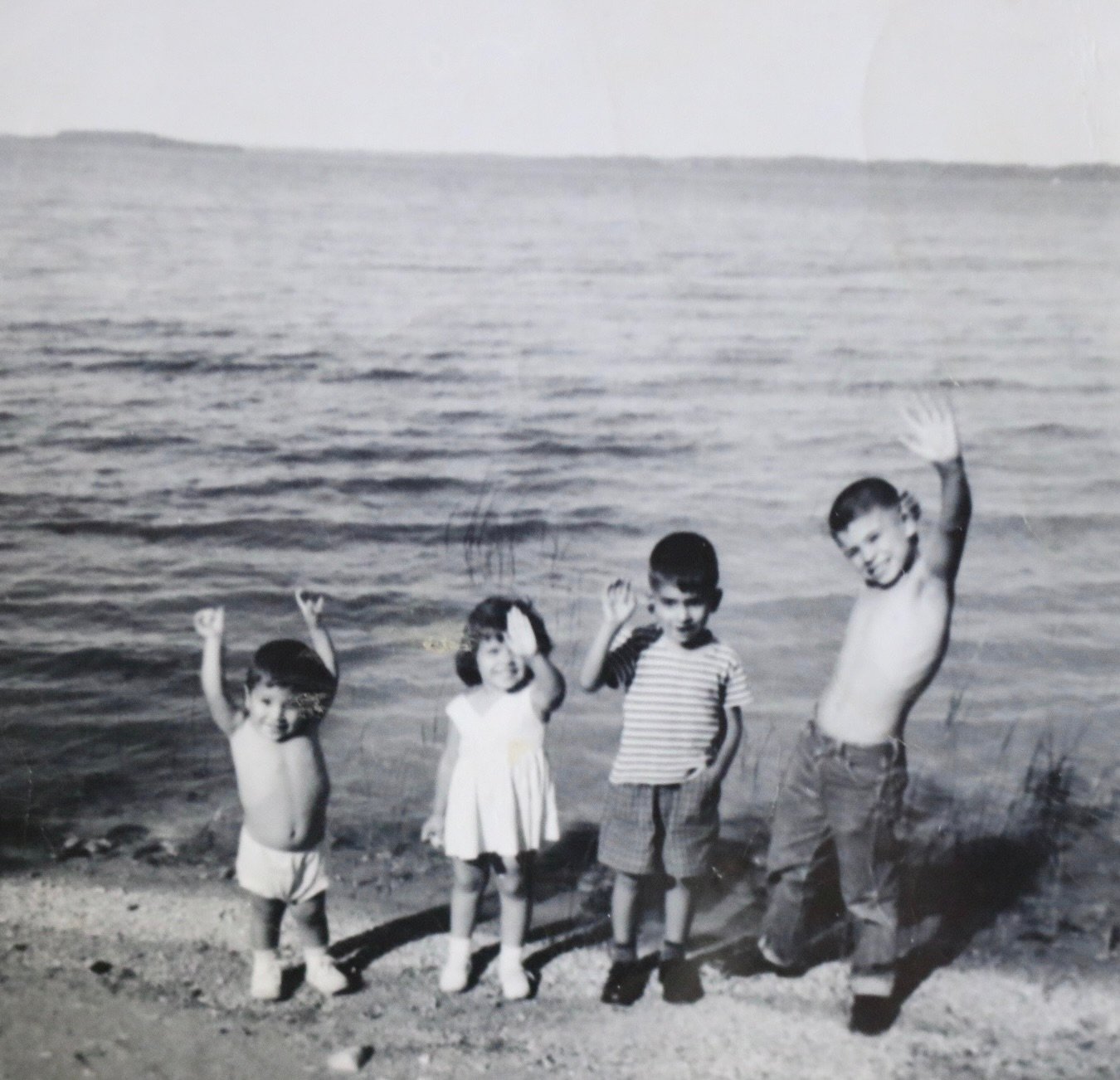 Four children standing in front of the lake waving