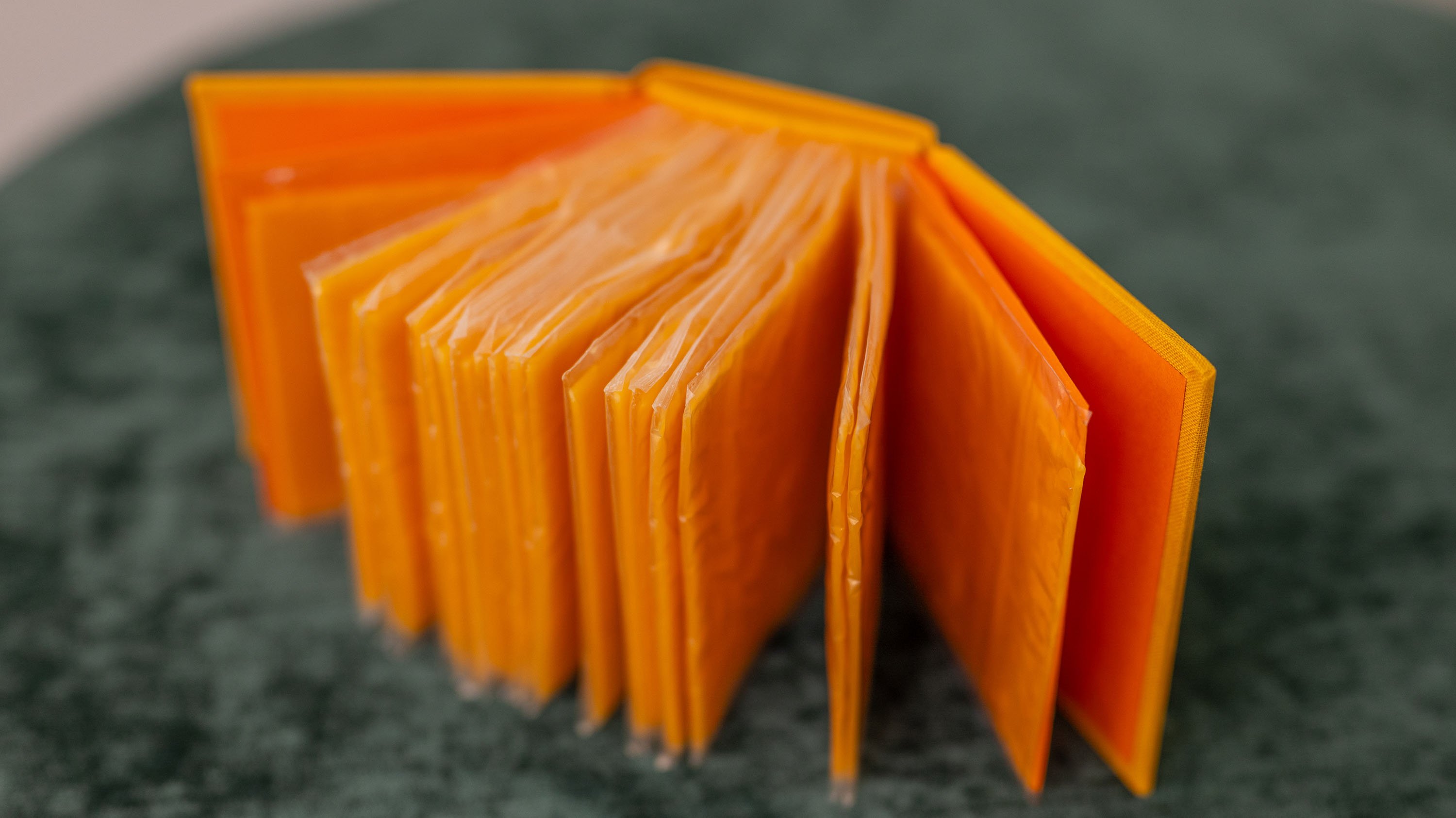 20 packs of sliced cheese packaged in clear plastic that have been arranged into a book. This image shows the book open, with the 'pages' of cheese splayed out. 