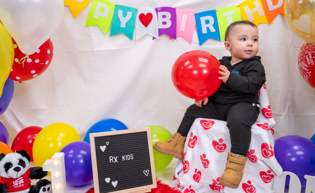 Child holds balloon with Rx Kids branding. 