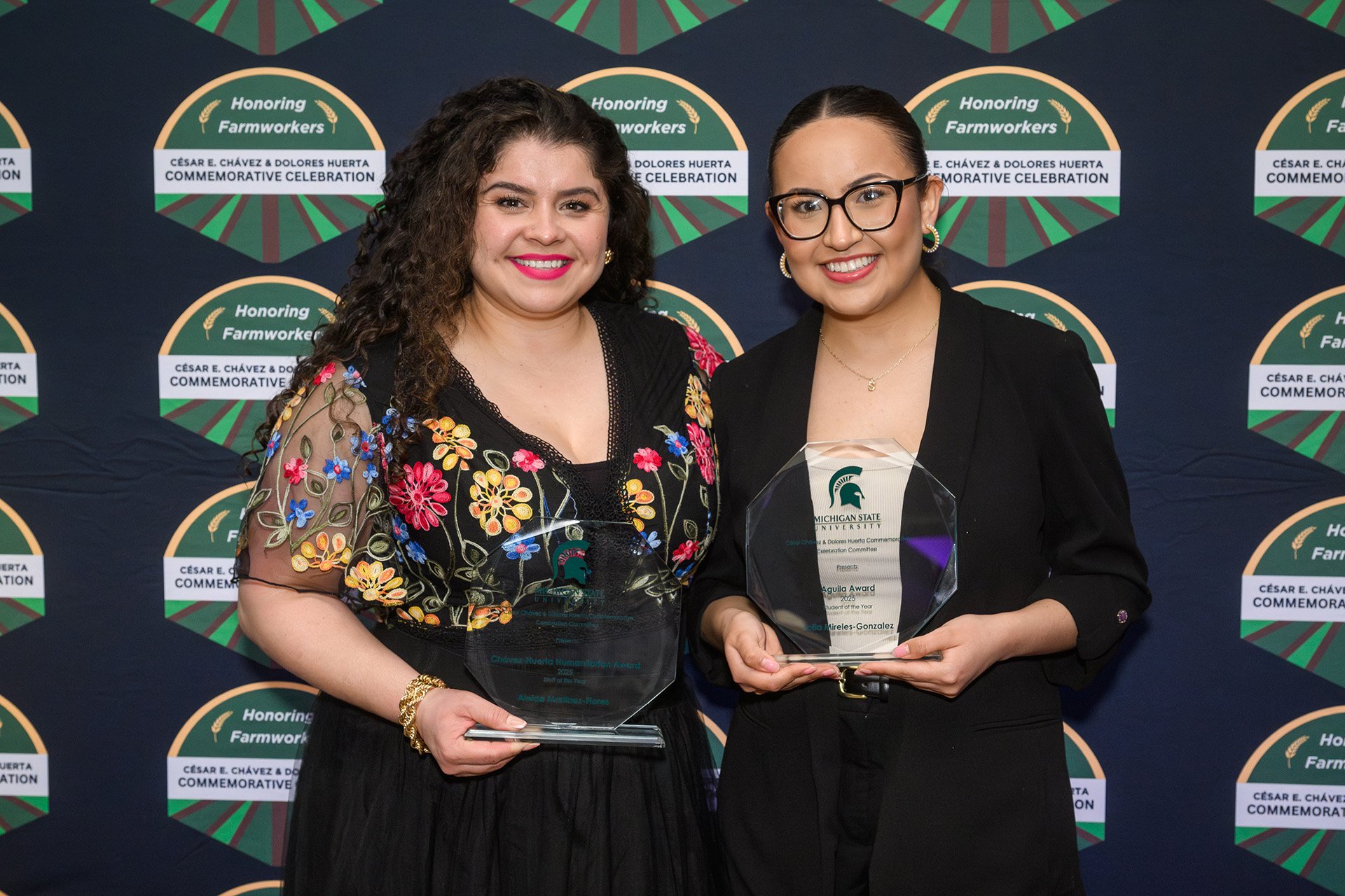 two award recipients in front of a photo backdrop