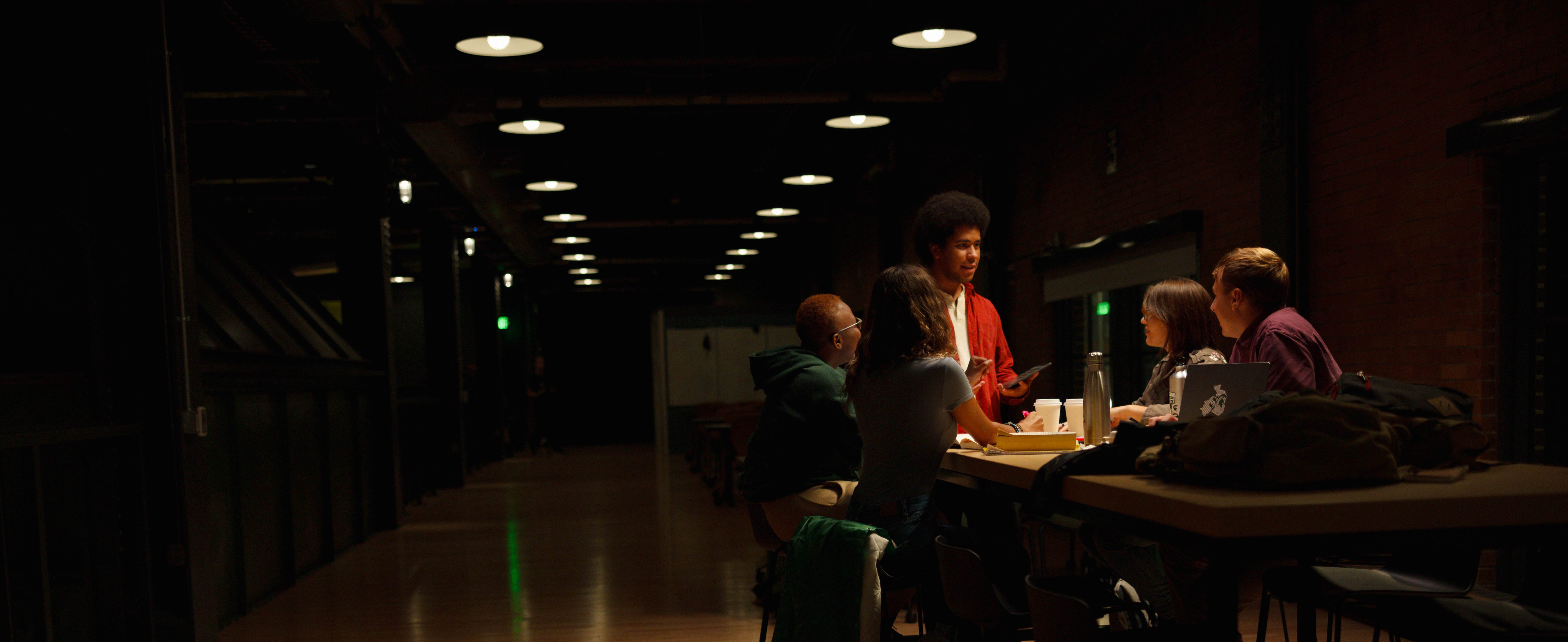 Group of students in a dark room highlighted by a light.