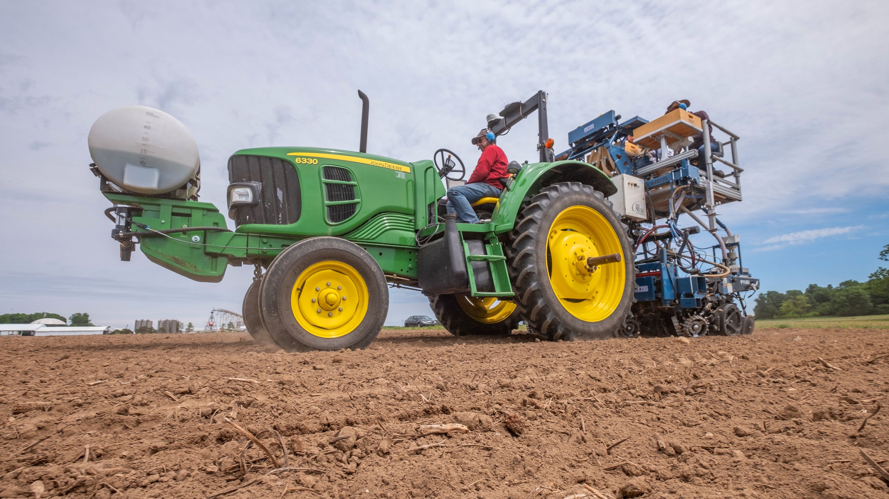 Person using farm equipment to plants seeds in a field