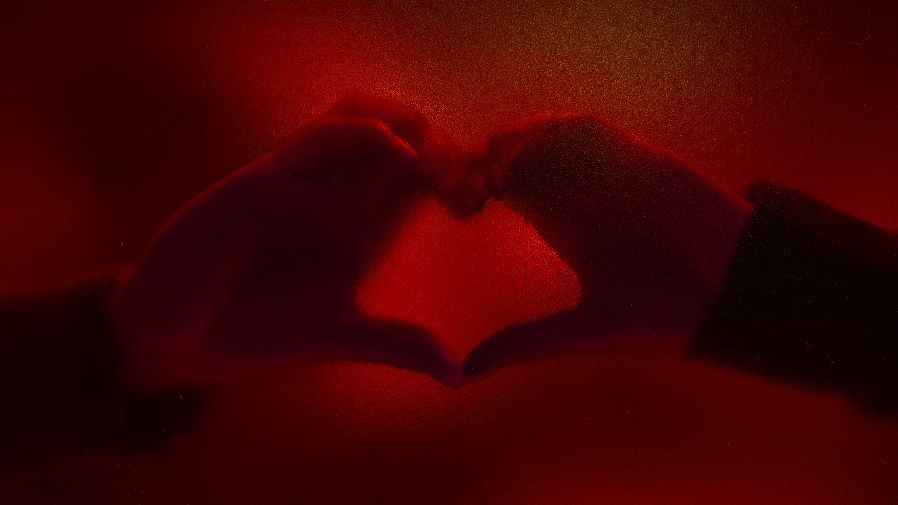 Two hands forming the shape of a heart behind red glass