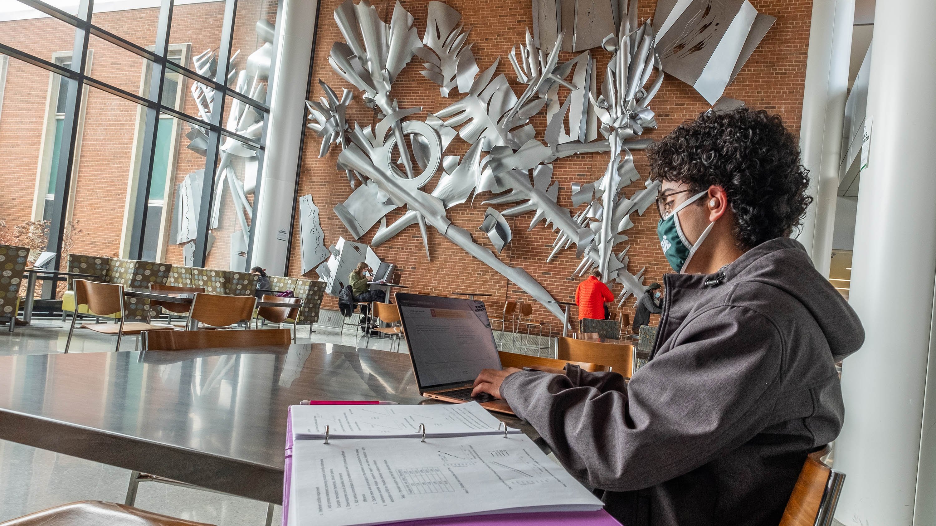 Students studying in the atrium of the Molecular Plant Sciences building with the wall art 'Cadence' in the background