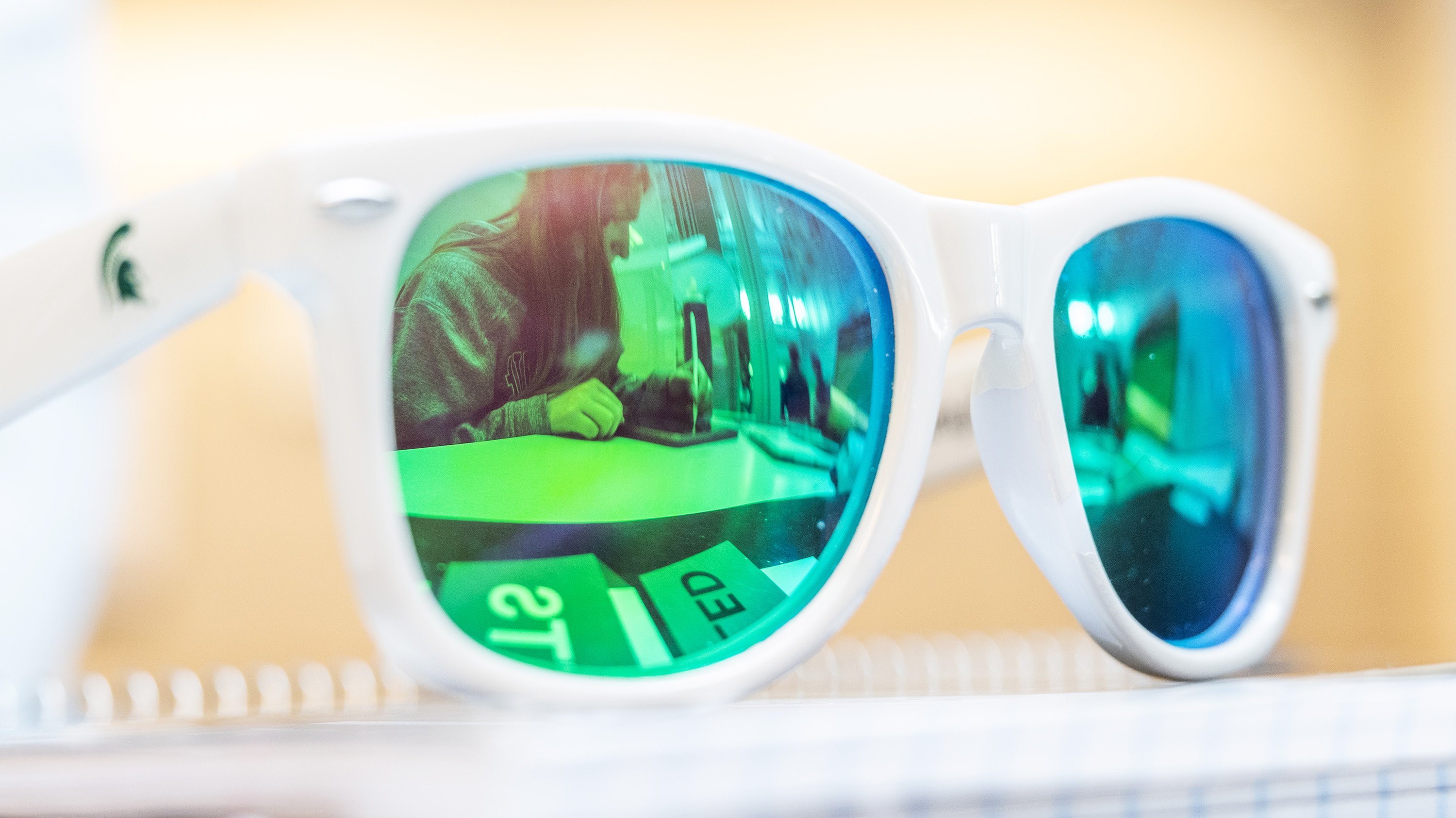 Green-tinted sunglasses with student studying in relfection