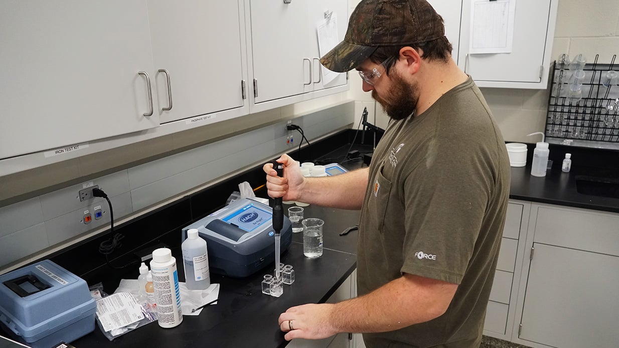 A worker uses a large pipette to add water to small jars.