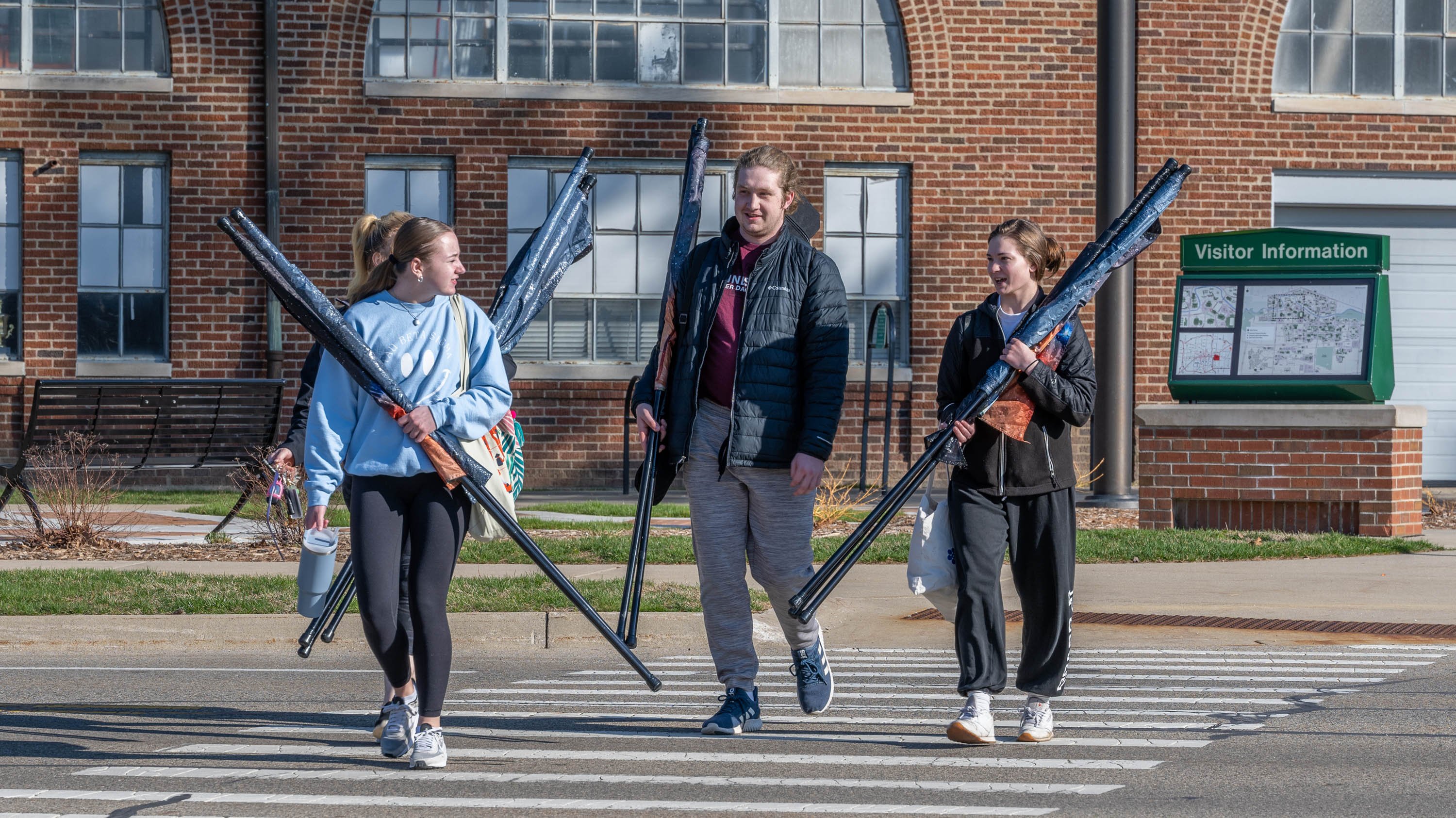 Three members of color guard walking with furled flags