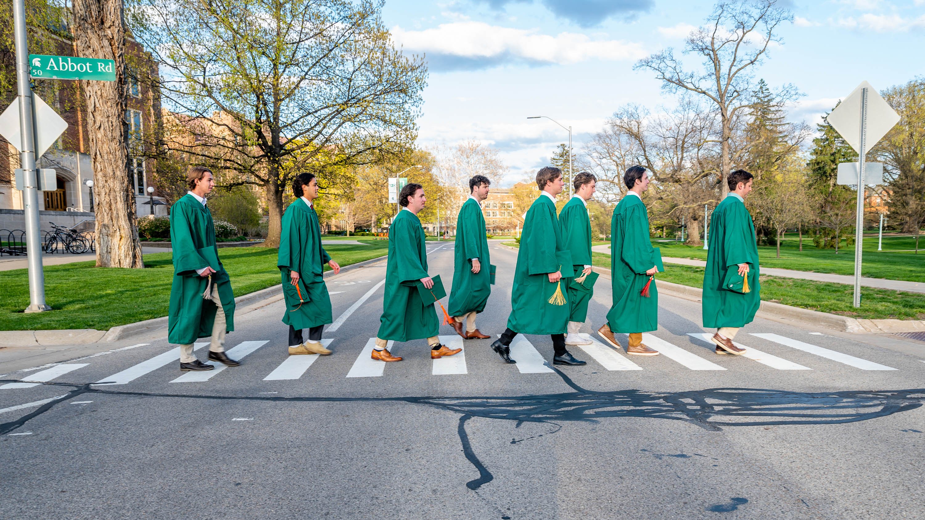 Students in graduation gowns walking through crosswalk