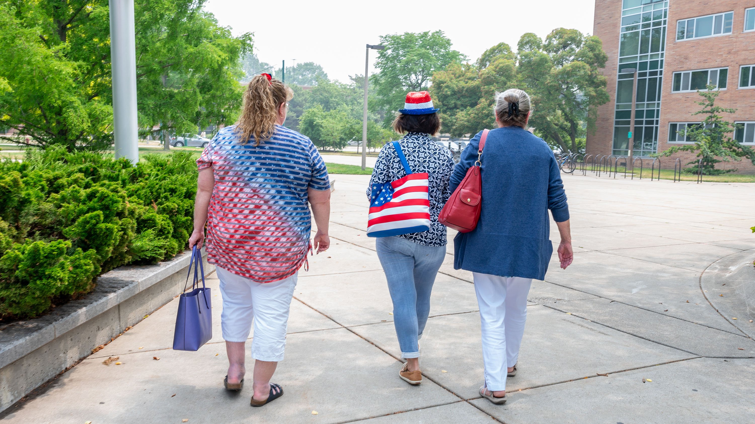 Three people wearing red, white and blue walking on campus