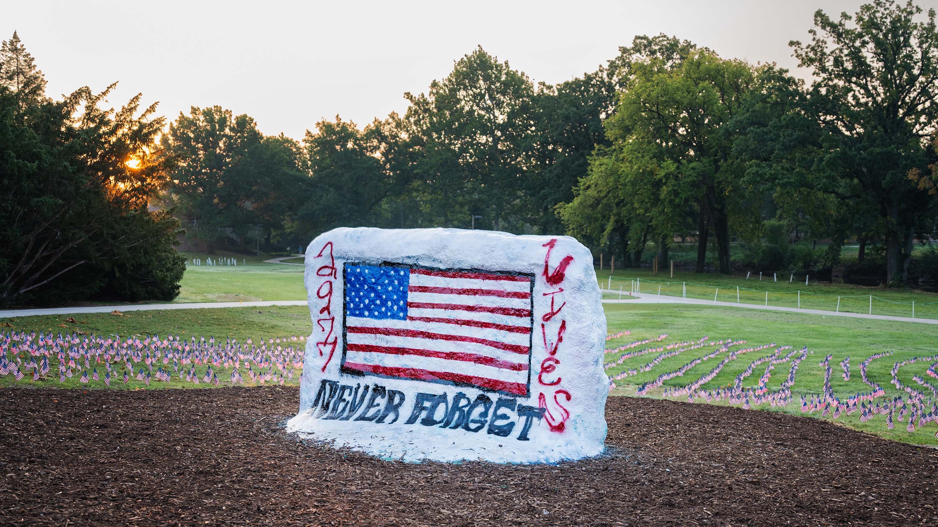 MSU Rock painted with American flag and '2,977 lives, never forget' in front of field of American flags