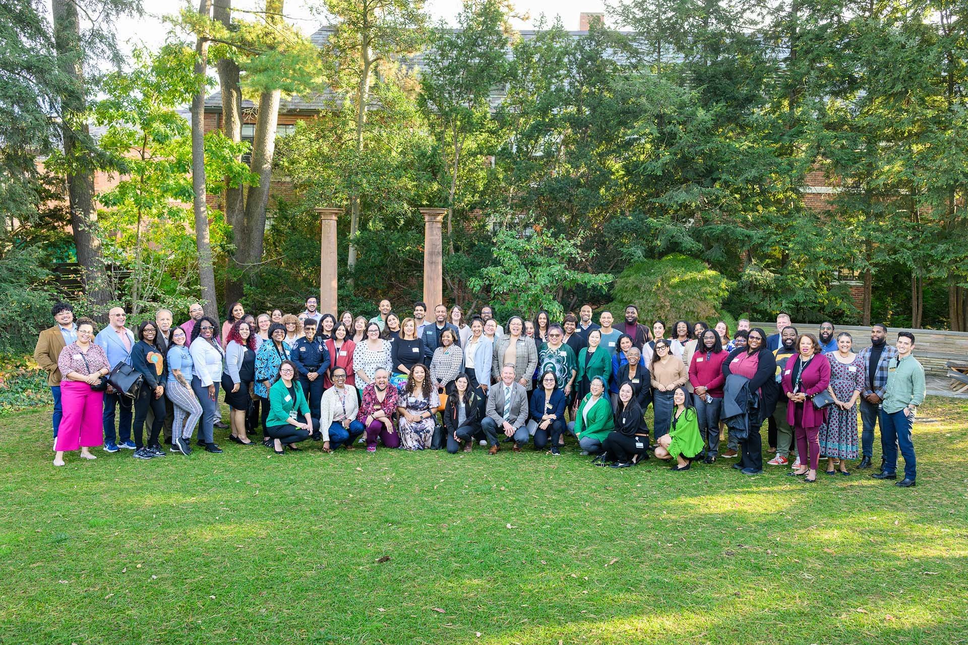 A photo with a lot of individuals posing outside among green grass and trees.