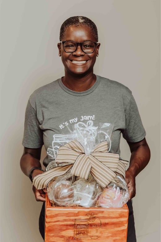 An individual holds a basket with a large bow that holds various artisan treats.