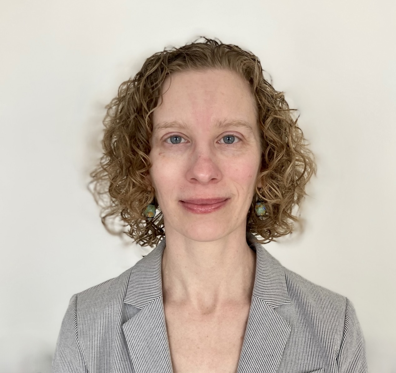 A headshot of Ashley Shade, who’s smiling and wearing a black-and-white striped suit jacket.
