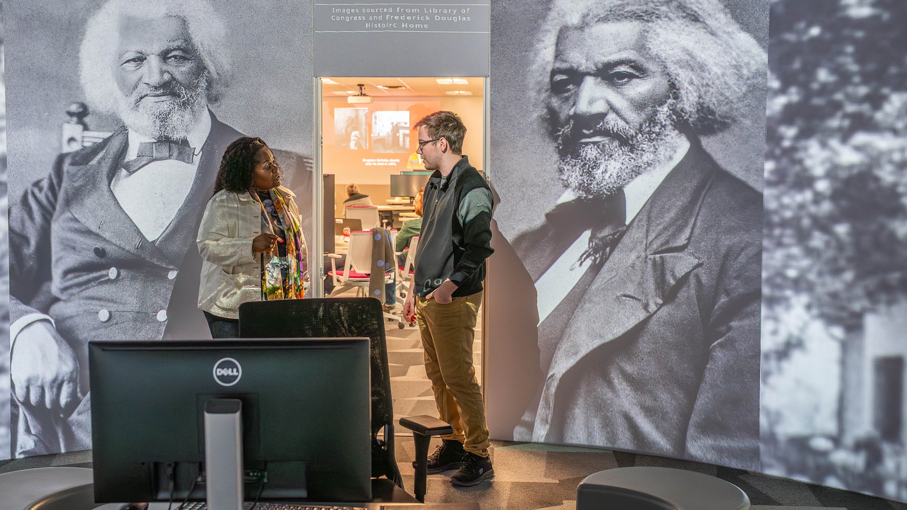Two people in a room with images of Frederick Douglass projected on the wall