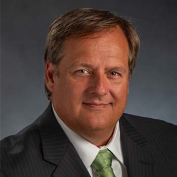 Todd Carter  profile photo, shown wearing a dark suit, white shirt and green tie