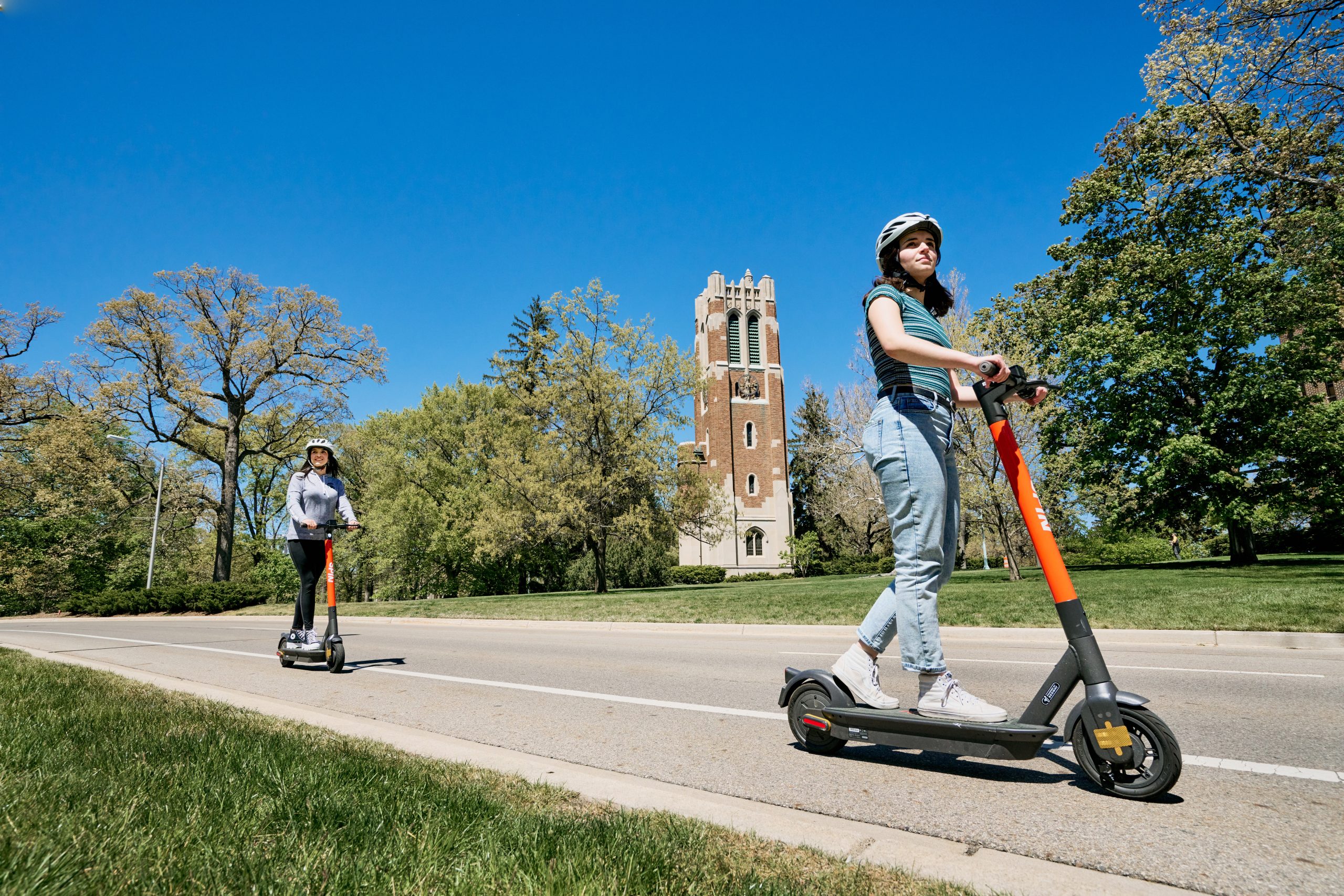 Two students on SPIN scooters riding around campus