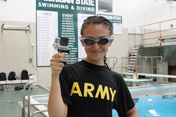 Person with an ARMY t-shirt and goggles on holding a go-pro camera at an indoor pool