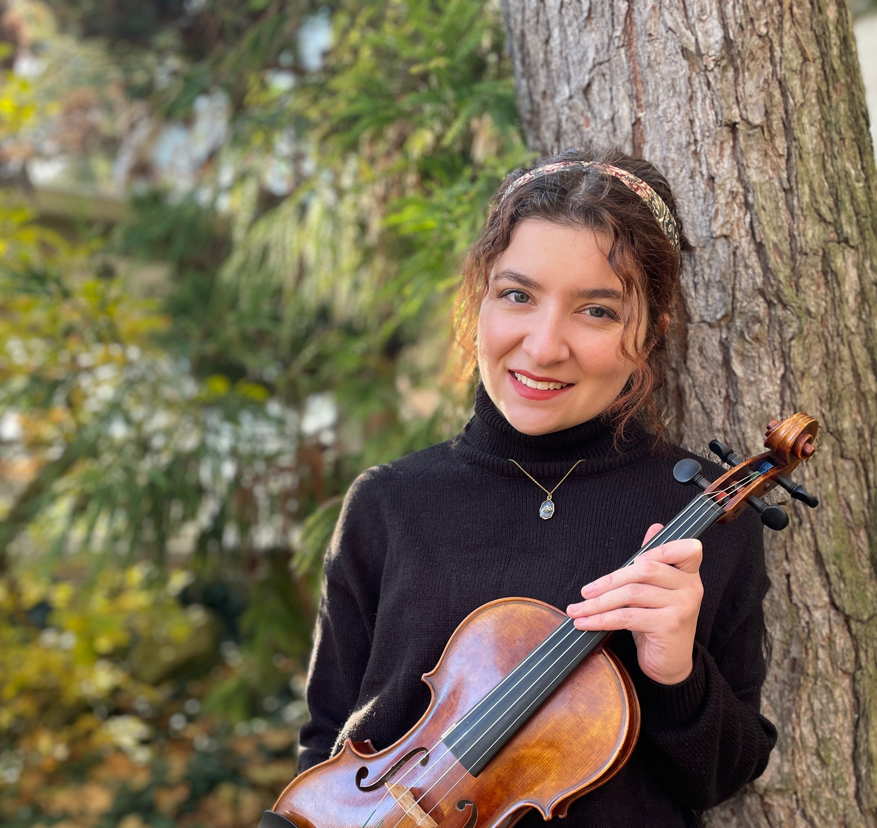 woman holding a violin standing in front of a tree