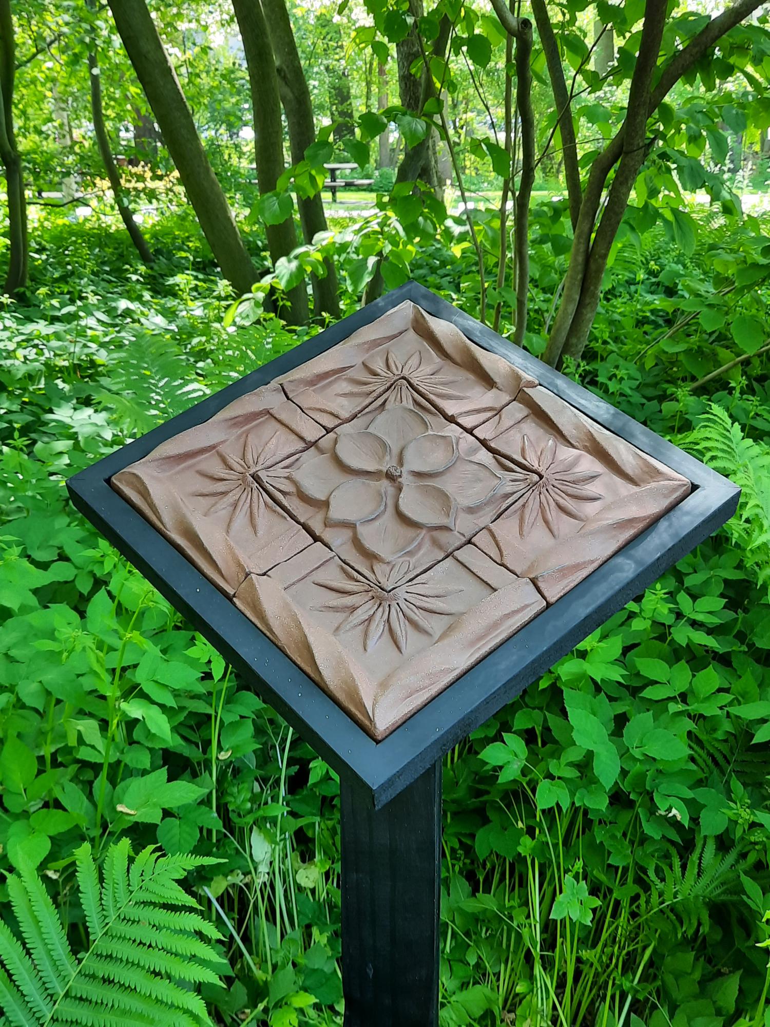 ceramic tile artwork on a post in a garden