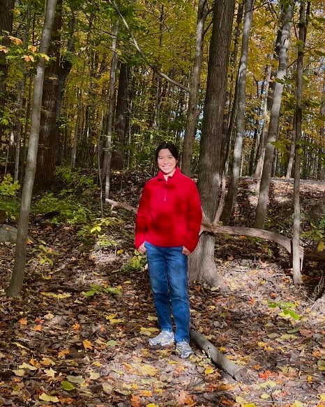 woman wearing a red jacket and denim standing in the forest