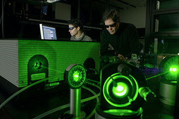 Two people wearing protective in a dark room with green lasers set up in an experiment.
