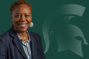 Headshot of Kathy Charles, senior director for Faculty and Academic Staff Affairs, from the shoulders, smiling a navy blue blazer and a blue and white striped shirt, in front of a green background featuring a Spartan helmet logo.