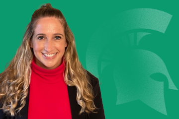 Headshot of Julie Fusi, executive staff assistant for Faculty and Academic Staff Affairs, from the shoulders up and smiling, wearing a black blazer and red shirt in front of a green background featuring a Spartan helmet logo.