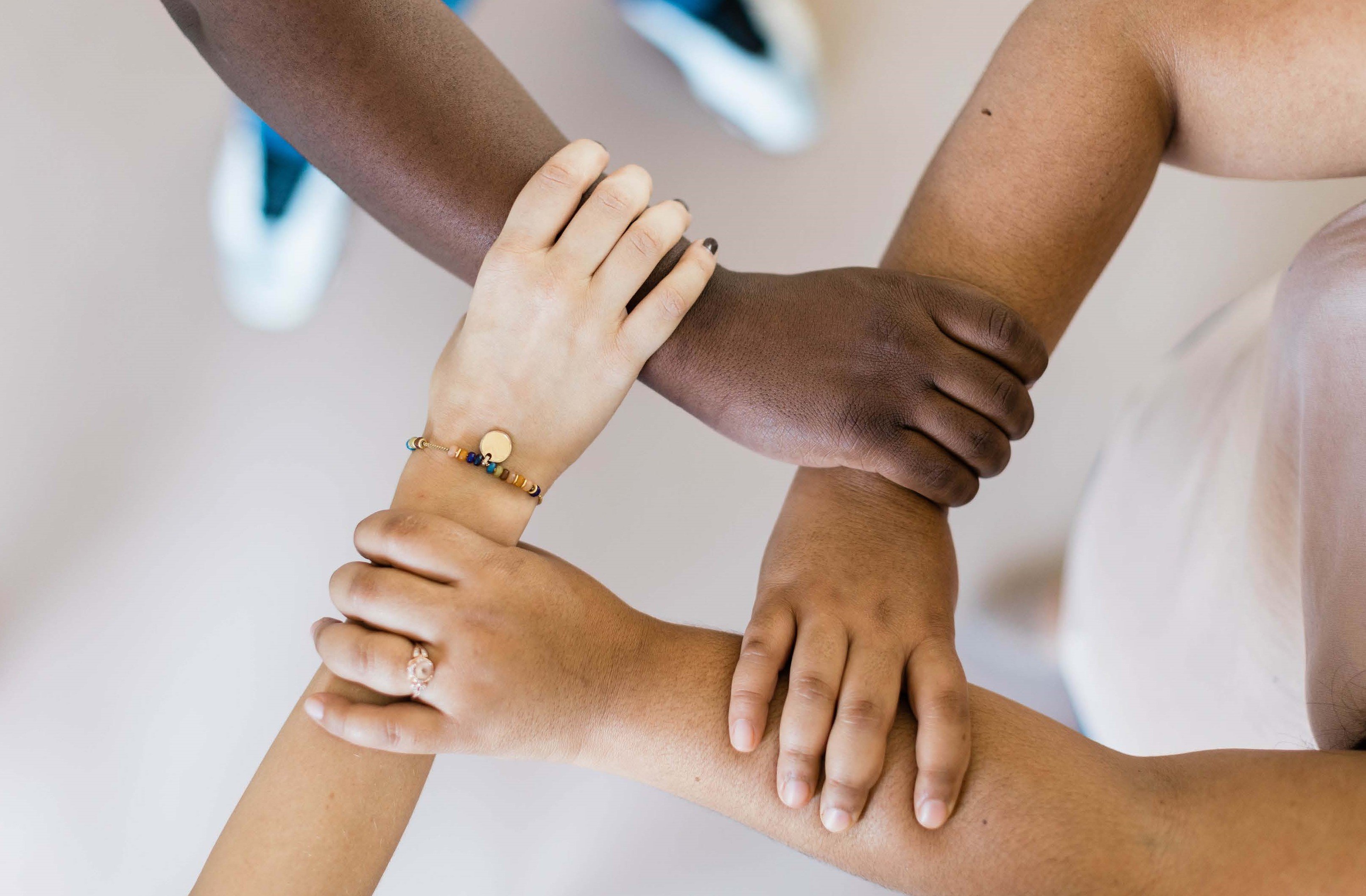 four hands of different people grabbing each other's forearms