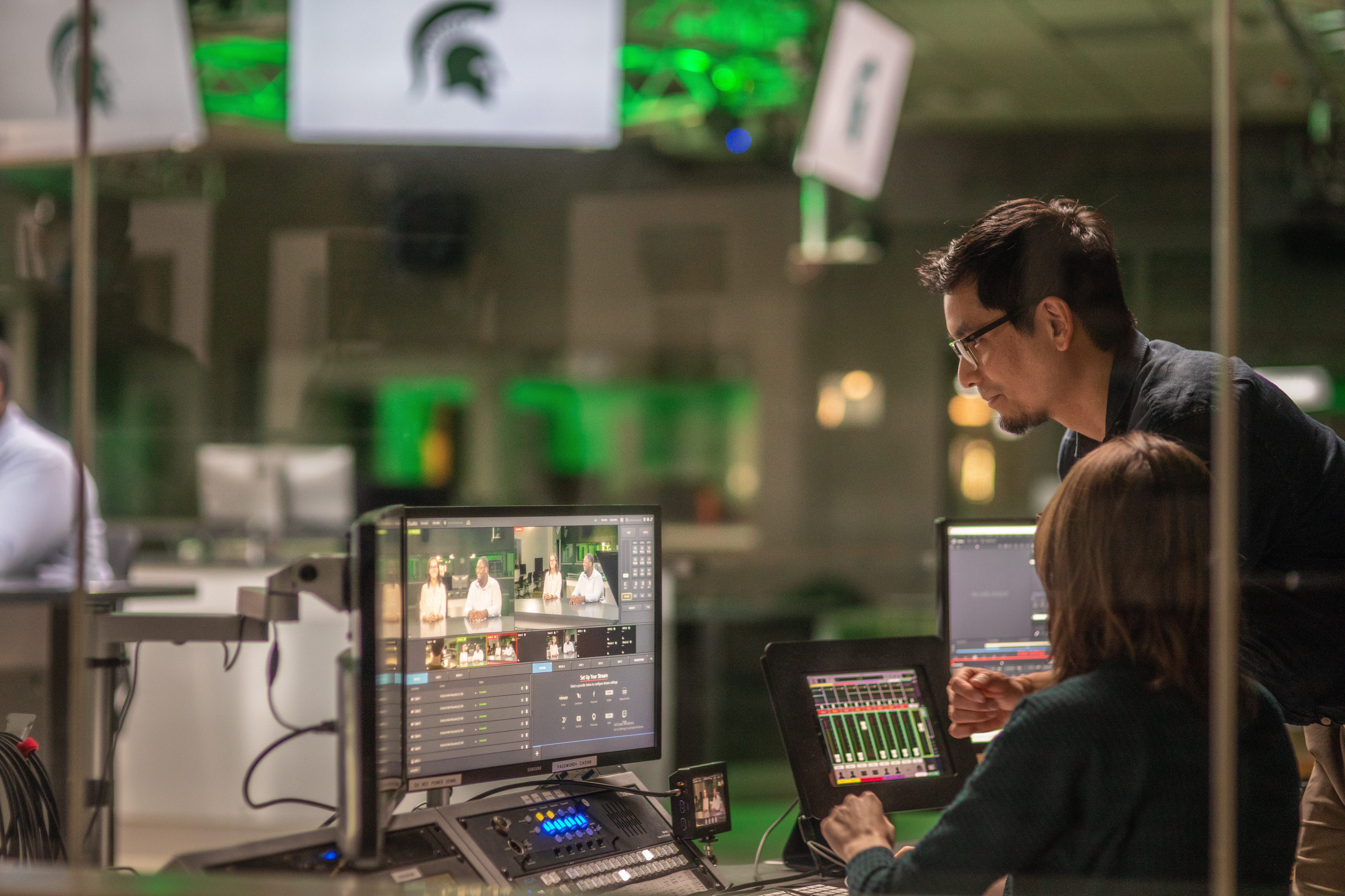 Students work in a WKAR studio. Video editing screens sit on a desk in front of them.