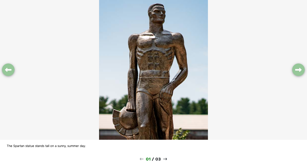 A screenshot of a carousel component using the Center Portrait Aligned variant. The photo appears in the center with a portrait orientation. The caption line and pagination arrows appear below the photo. In this slide, a photo of The Spartan Statue is shown.
