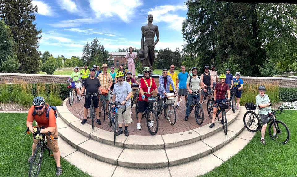 People on bikes standing in front of the Sparty statue.
