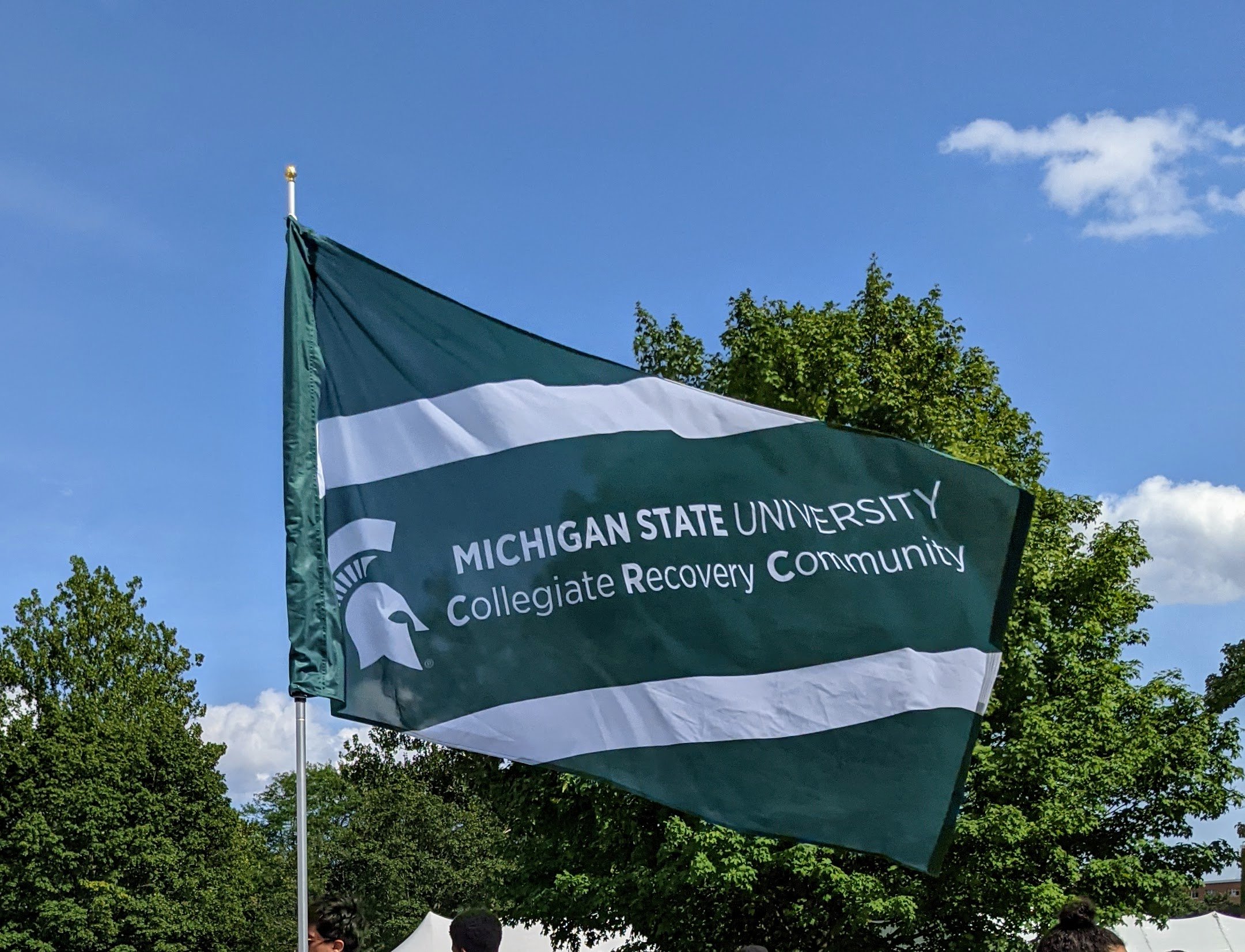 a flag outdoors that has a Spartan Helmet and has text that reads "Michigan State University  Collegiate Recovery Community"
