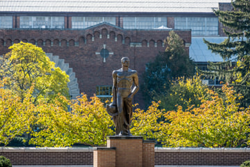 Sparty statue with tall brick building and bright trees