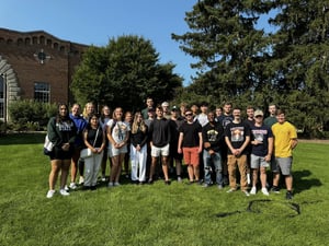 A group of students gathered together looking at the camera and smiling in front of Dem Hall on MSU's Campus