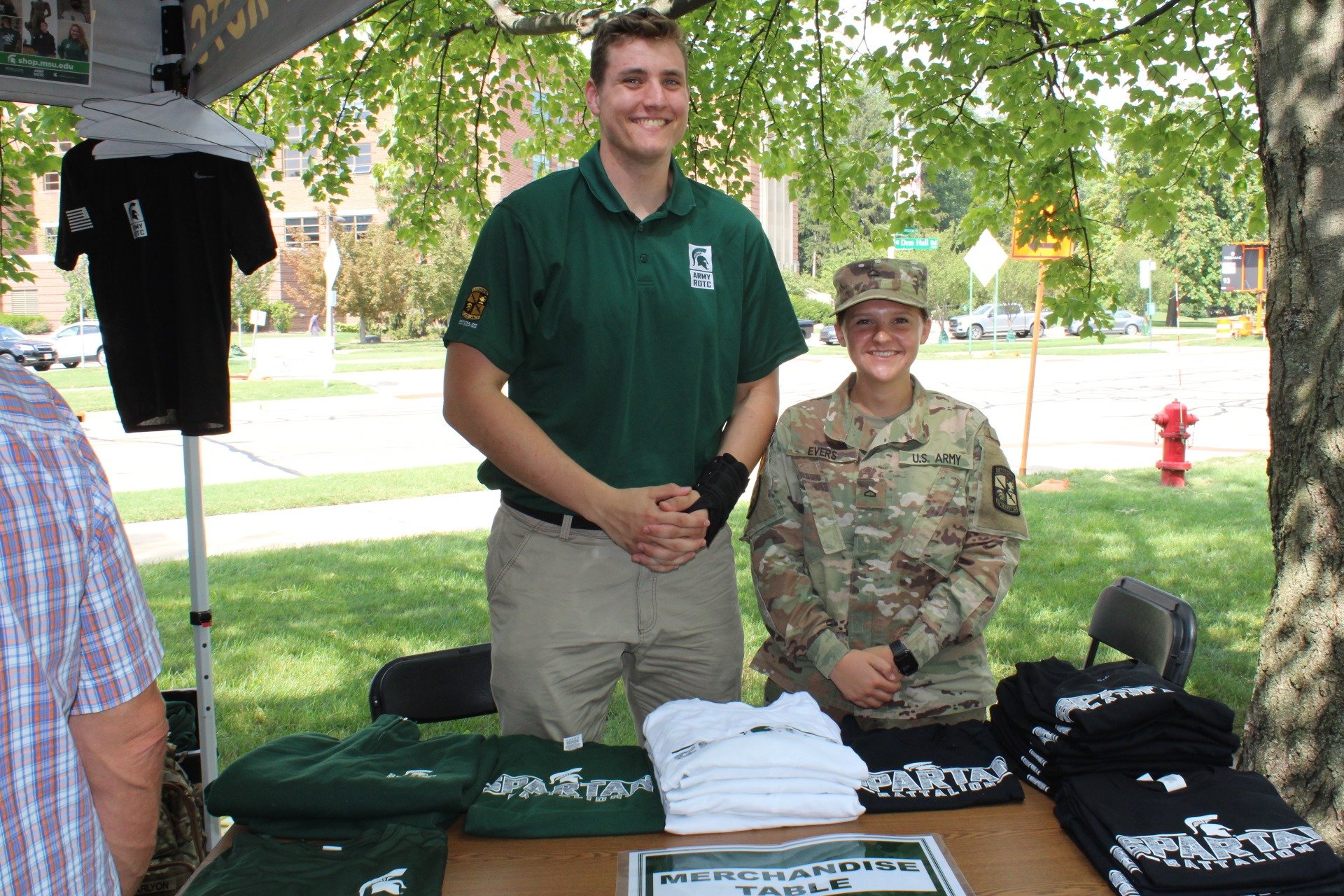 Two cadets standing behind a table full of Army ROTC shirts