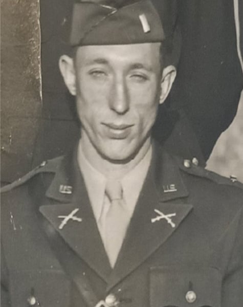 Black and white portrait image. Subject is wearing a military uniform with visible medals. They are standing in a group of other people.