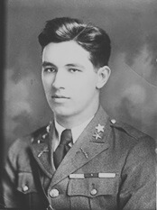 Portrait photo in black and white. Subject is wearing a military uniform with visible medals with dark short hair against a grey backdrop.
