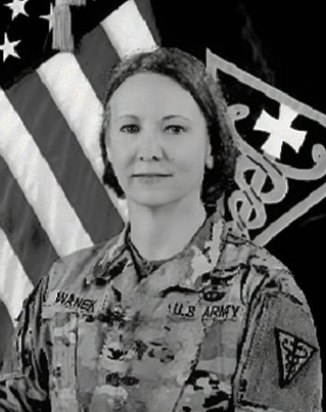 Black and white portrait photo. Subject is wearing military fatigues and is set against an American flag. 