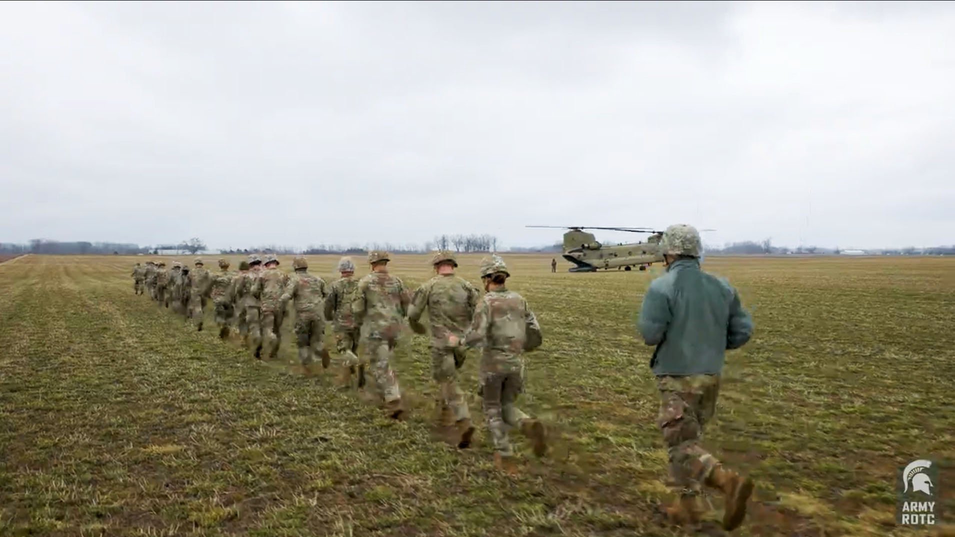 cadets running in a green field with a helicopter on the grass in the background