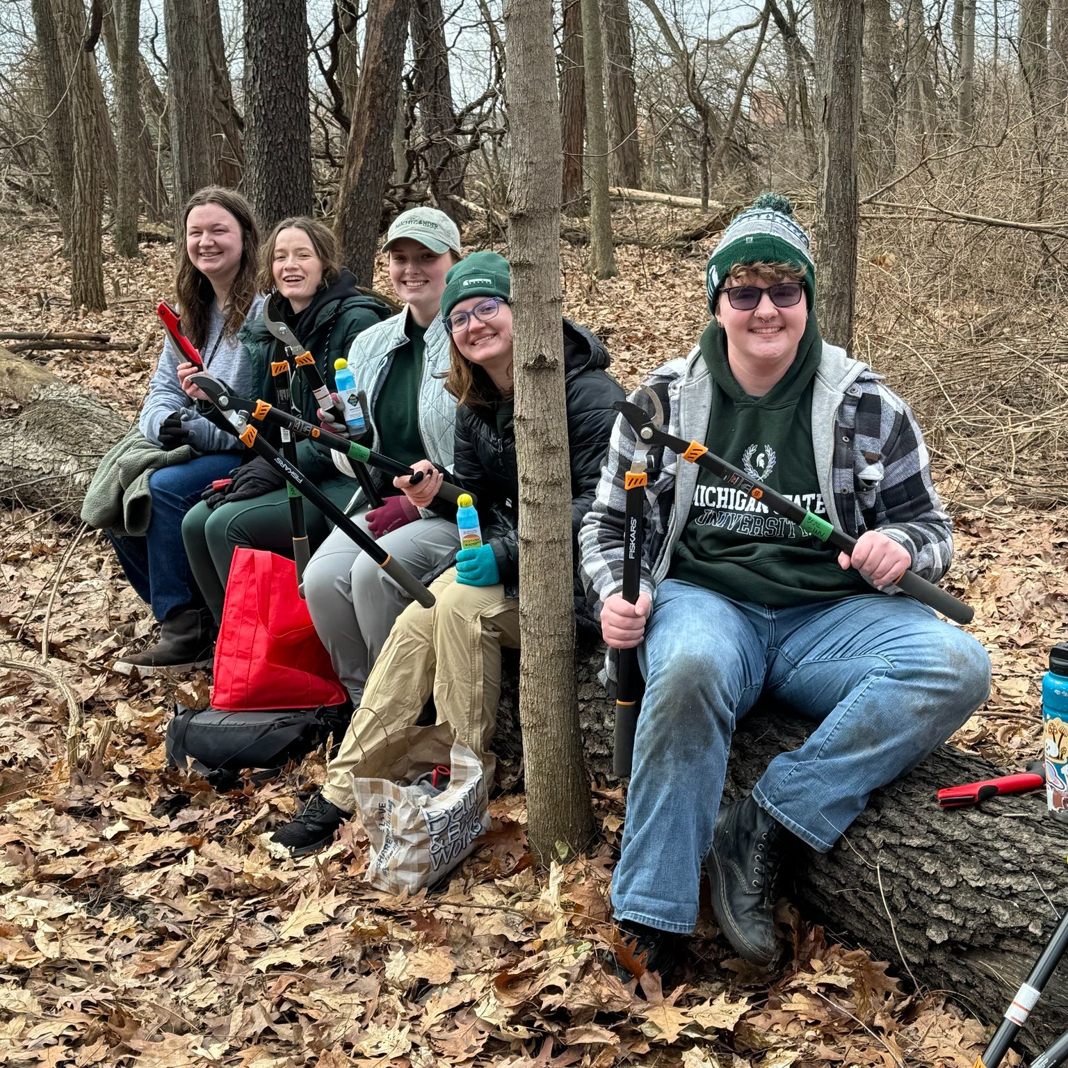 a group of people dressed in warm clothes sitting on a log in a forest